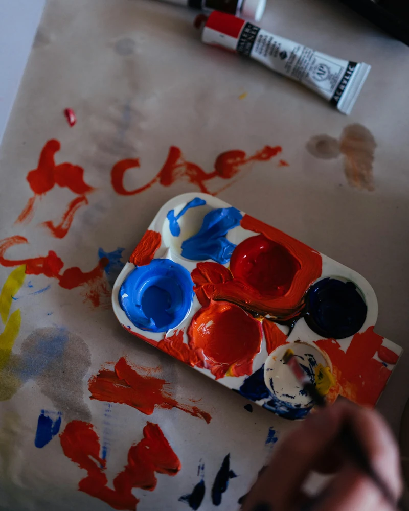 Tavolozza con colori rossi e blu, pennelli e tracce di pittura.