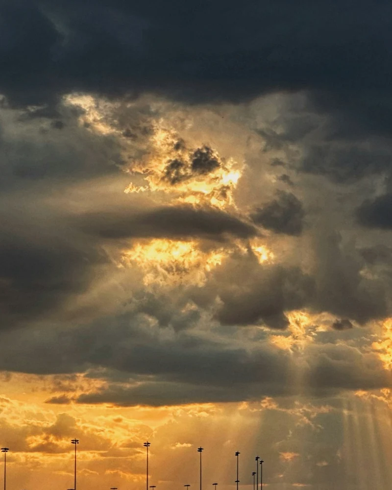 Raggi di sole dorati attraversano un cielo di nuvole scure.