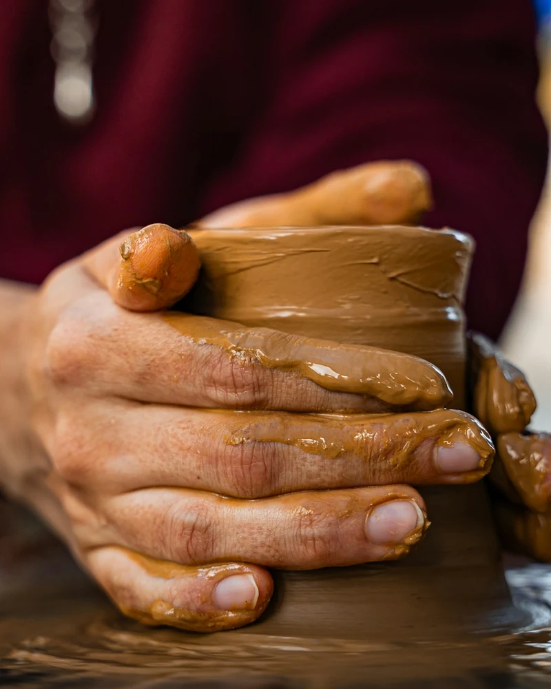 Mani che modellano un vaso di argilla su un tornio.