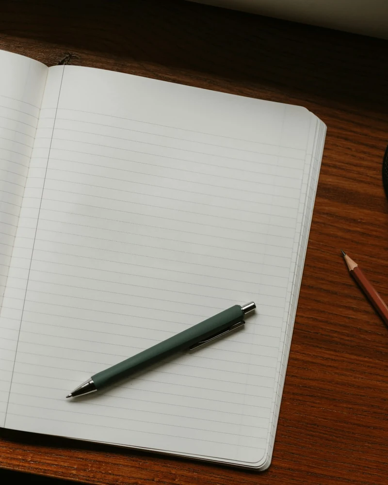 Quaderno aperto con una penna e matite su una scrivania di legno.